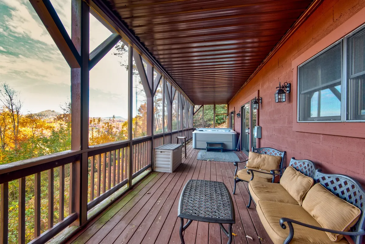 A bubbling hot tub sits on a wooden deck overlooking the scenic mountain landscape, with comfortable seating and a sturdy railing providing safety and comfort. The area is perfect for relaxing after a day of adventure, whether rain or shine.