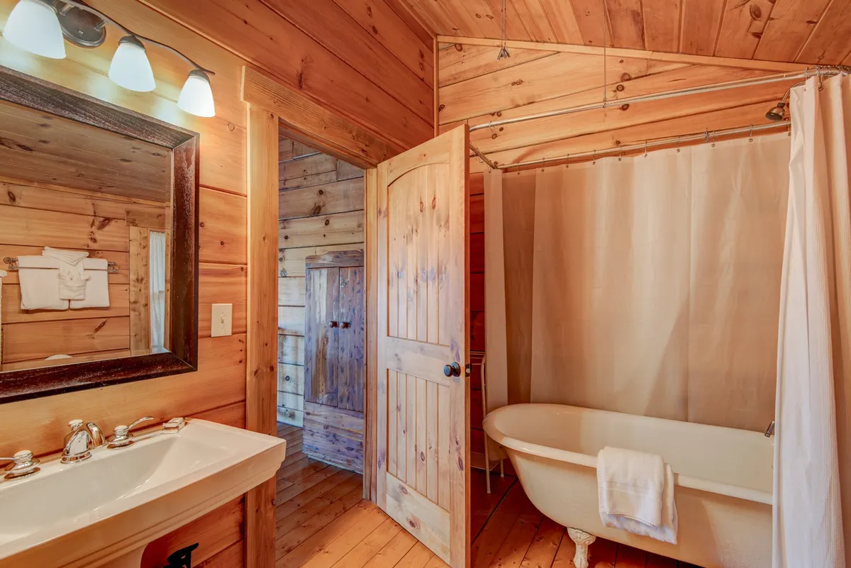 A cozy, rustic bathroom with a vintage clawfoot bathtub, wooden accents, and a classic mirror. The space feels personal and romantic, ideal for quiet relaxation after a long day.