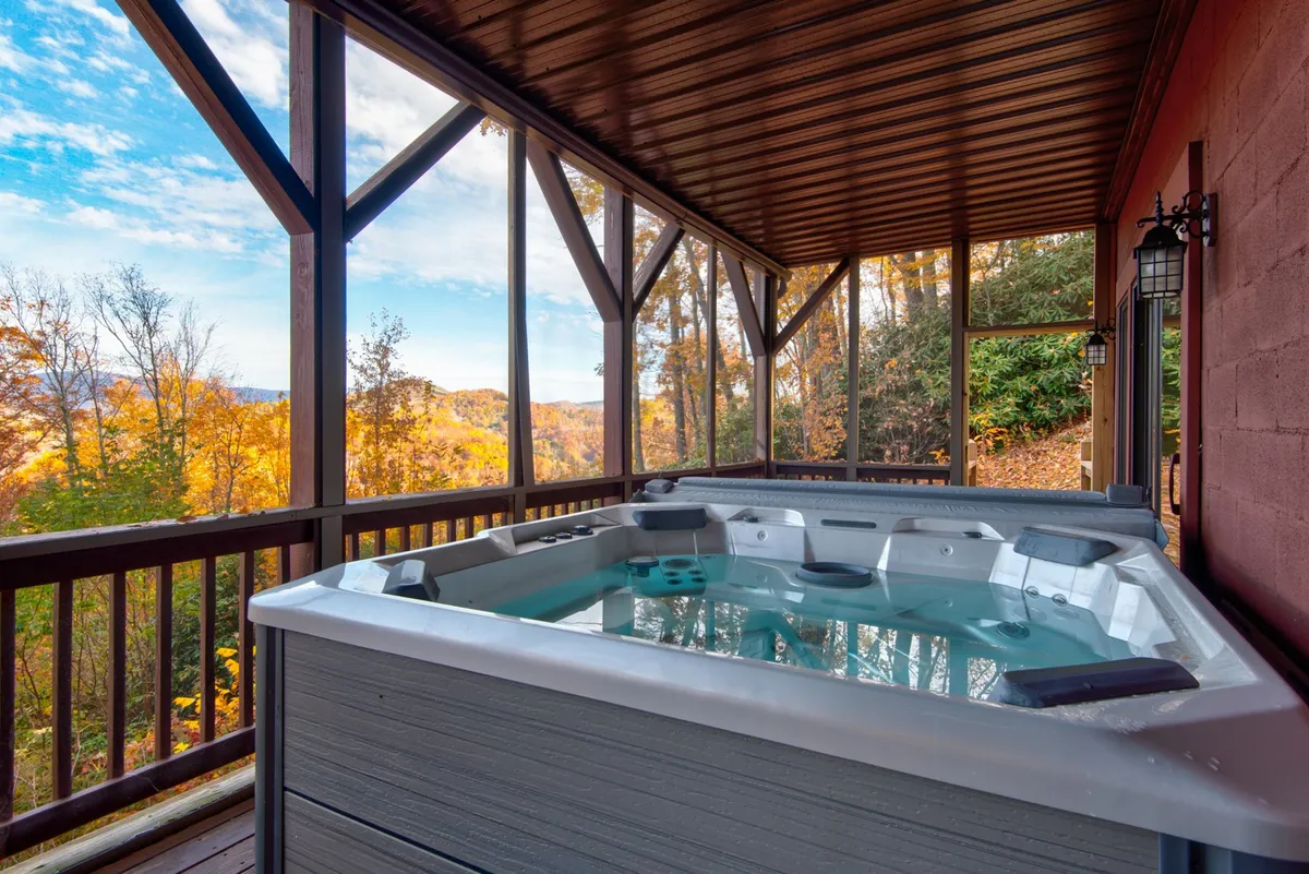 A covered outdoor hot tub sits beneath a wooden beam structure, offering panoramic mountain views and a tranquil setting for relaxation regardless of the weather. The inviting tub is surrounded by nature, enhancing the luxurious experience.