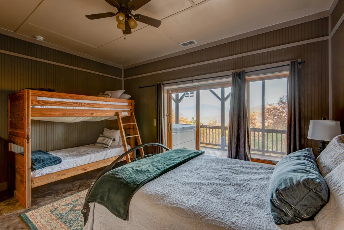 A family-friendly bedroom with a queen bed and a bunk bed. Large windows allow for natural light, and the bedding is textured and inviting. The space is warm and suitable for both adults and children.