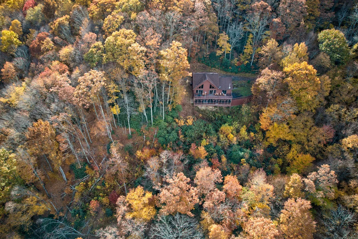 This exterior image highlights the house nestled among mature trees and vibrant autumn foliage. The surrounding natural landscape provides a sense of privacy and serenity, perfect for couples seeking a secluded retreat. The peaceful outdoor environment suggests opportunities for hiking, enjoying the crisp mountain air, and relaxing on the porch while soaking in the tranquil beauty.