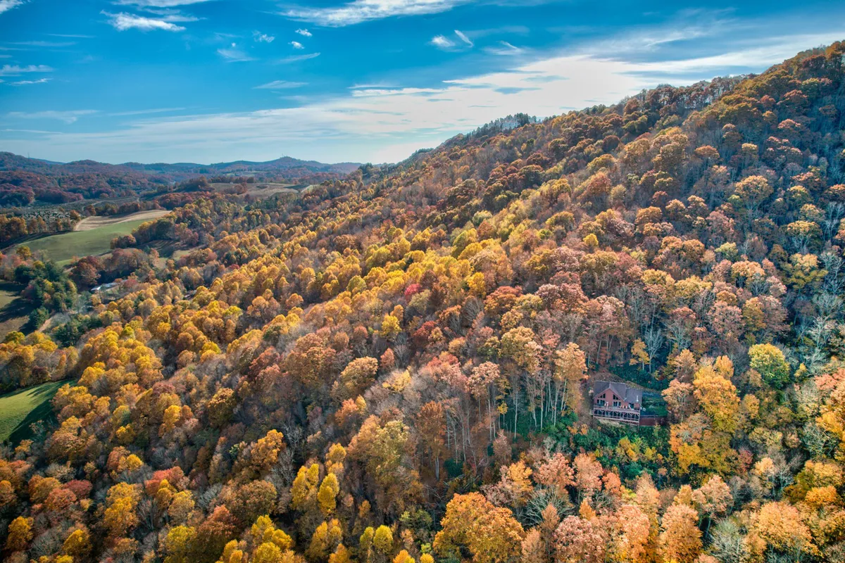 A wide view of the house nestled in a rolling landscape, surrounded by colorful autumn trees. The scene captures the expanse of the property and the tranquil, scenic setting, perfect for group hikes and nature exploration.