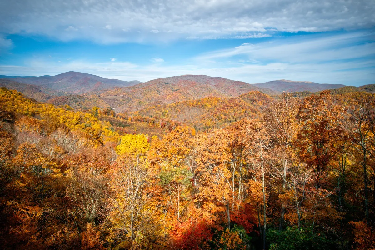 A breathtaking view of rolling mountains, a vast sky, and vibrant autumn foliage. The scene evokes a sense of adventure and the awe-inspiring natural backdrops available to guests, reinforcing the idea of exploring trails, waterfalls, and scenic vistas as described in the section.