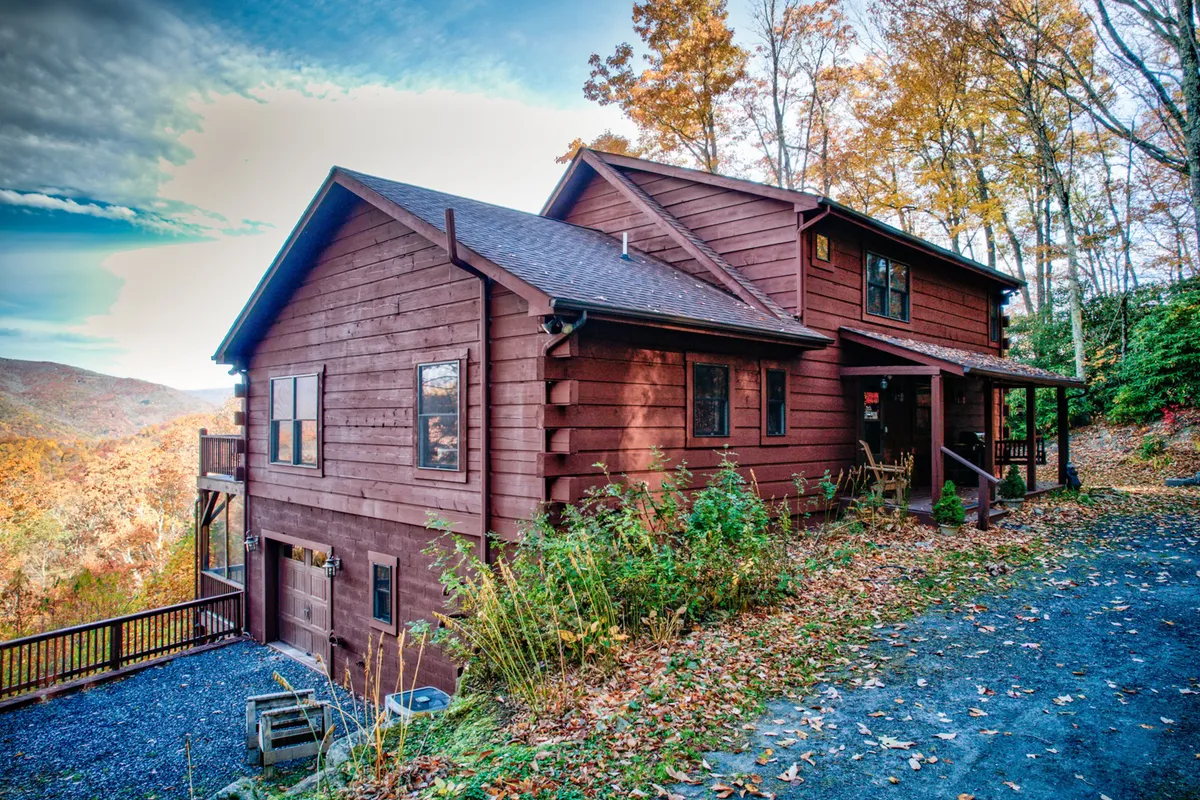 This image showcases the wooden exterior of the house surrounded by vibrant autumn foliage, with a spacious deck area visible. The deck offers seating and opportunities for outdoor gatherings, while the fall colors highlight the mountain setting.