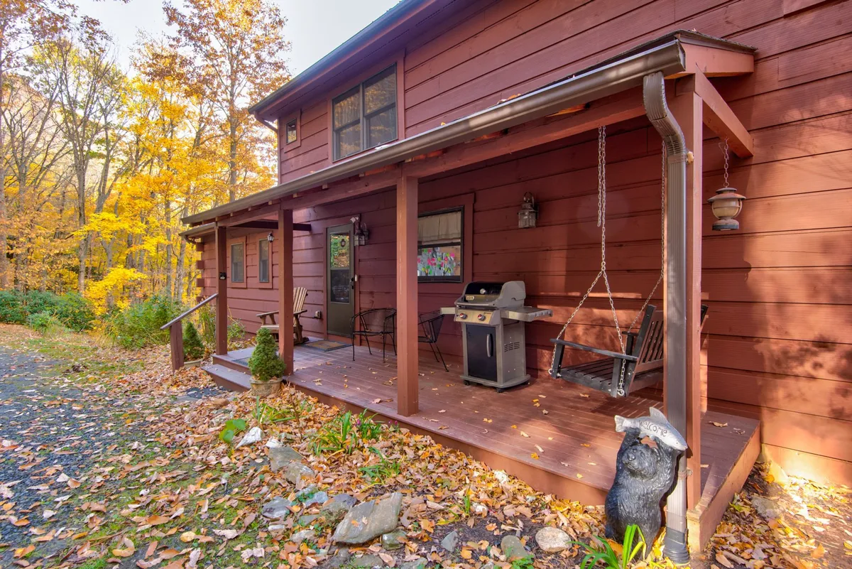 An inviting porch scene with a swing, grill, and a decorative bear statue, set against the backdrop of autumn foliage. This area is ideal for morning coffee, casual grilling, and intimate conversations in a cozy mountain setting.